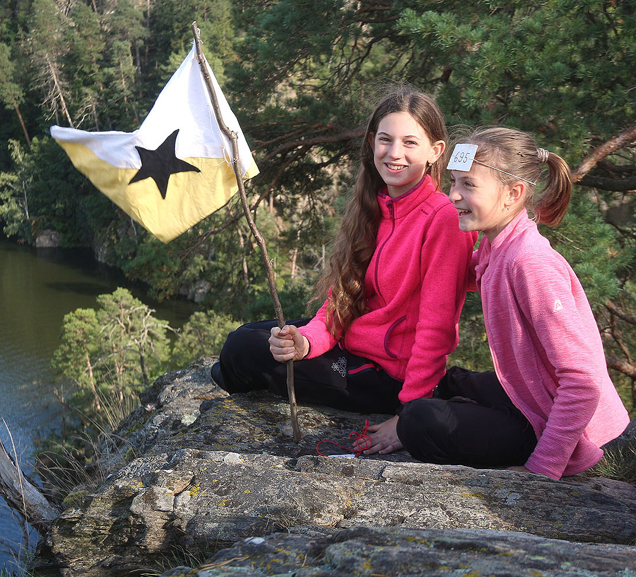 Vítězná děvčata se svojí vlajkou slaví na skále nad vodami jezera.