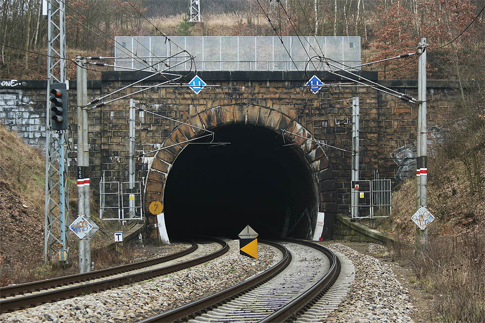 Jižní portál Havlíčkobrodského tunelu. Celý tunel se nachází v poměrně prudkém oblouku nad řekou Sázavou. U koleje 92* (vlevo) stojí opakovací návěstidlo OPřS92, opakující návěst návěstidla S92 za tunelem, v místě, kde z <a href="/Tema/Železniční trať Brno – Havlíčkův Brod">hlavní trati do Brna</a> odbočuje <a href="/Tema/Železniční trať Havlíčkův Brod – Pardubice">jednokolejná spojka trati do Pardubic</a> (směr odbočka Kubešův mlýn).