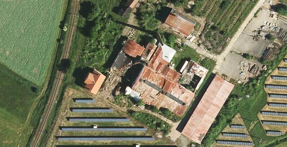Záběr na totéž místo v roce 2014 ukazuje zřícenou střechu jedné z hal a obklíčení solárních elektráren na původním poli.