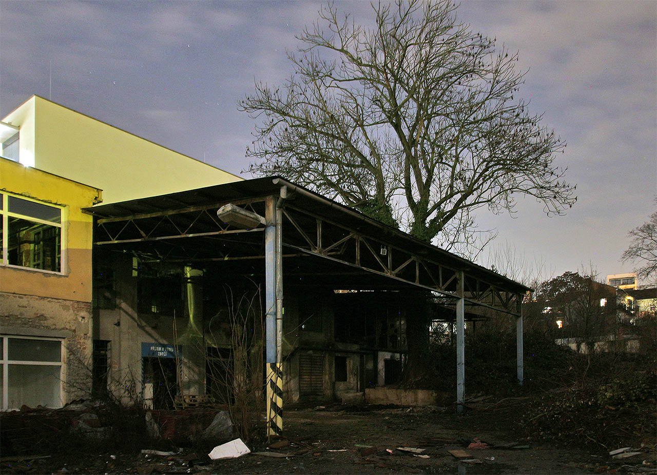 Na západní straně kryla vstup do továrny a manipulační plochu pro nakládku a vykládku zboží stříška s malým jeřábem. Nad nimi se sklání krásný strom, pamětník překotných dějin Horního Cejlu.